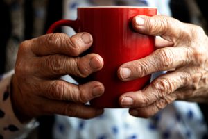Mains d'ne personne âgée tenant une tasse rouge