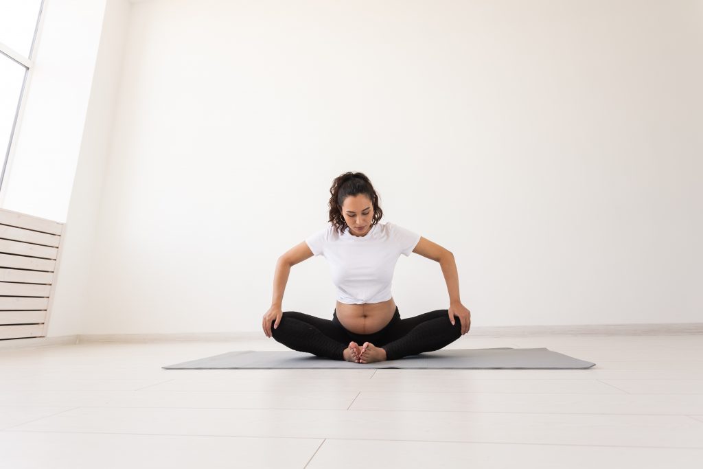 Femme enceinte assise sur un tapis de yoga et faisant un exercice